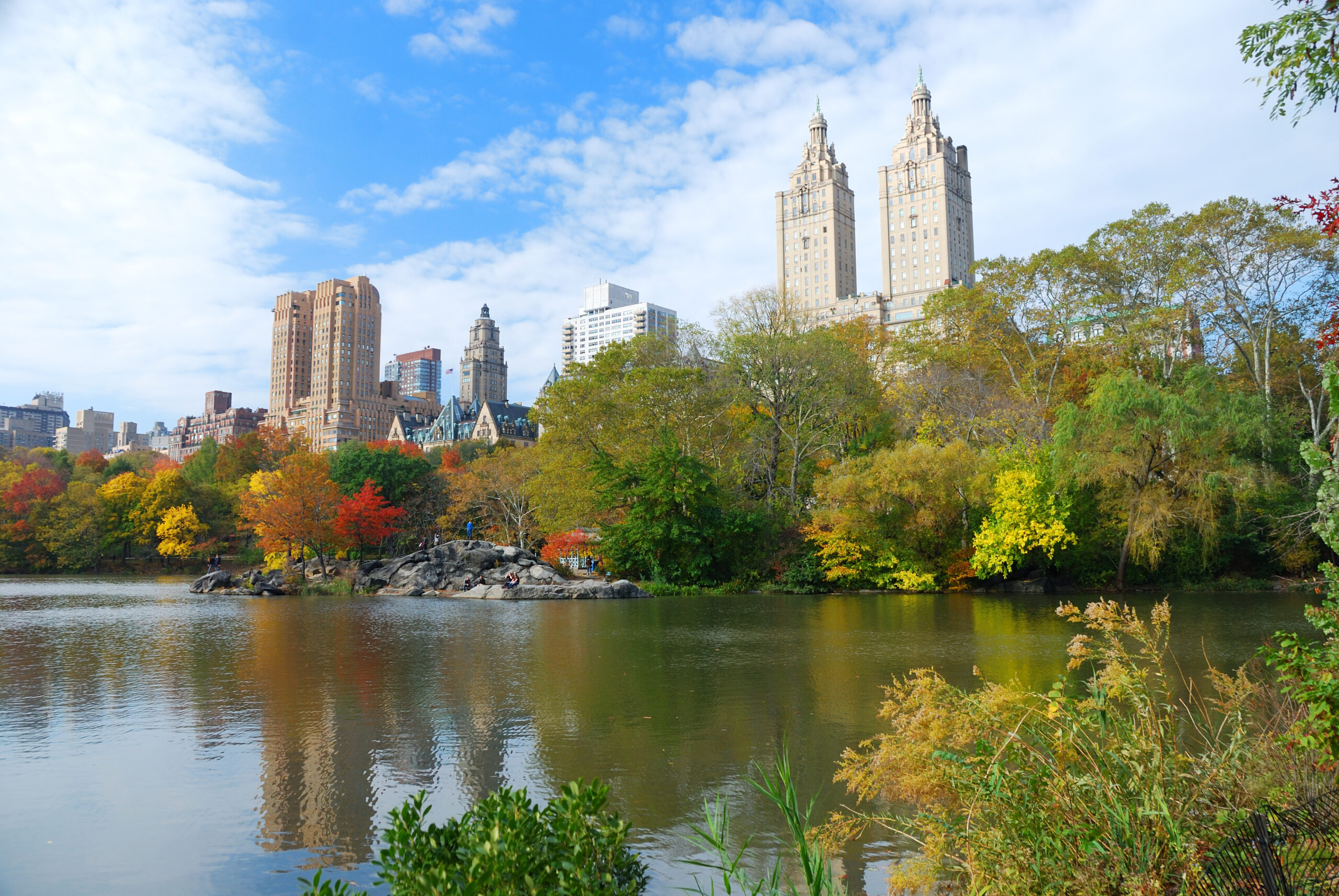 New York City Central Park in Autumn with Manhattan skyscrapers and colorful trees over lake with reflection.